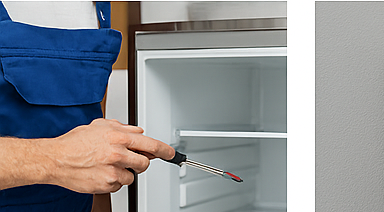 Technician repairing a refrigerator using tools for appliance maintenance.